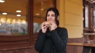 Genç bir lokanta, hamburgerci, koyu renk saçlı yiyici. Genç esmer bayan hamburgercinin tadını çıkarıyor..