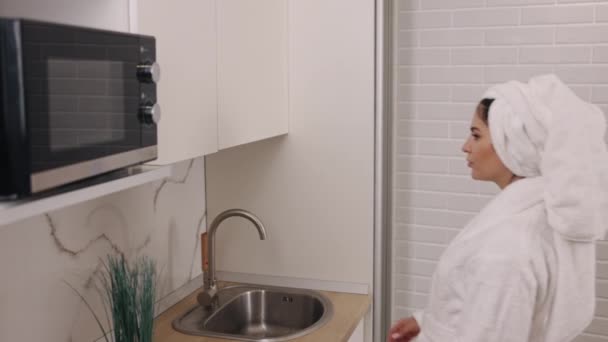 飲料水 キッチンウェルネス ハイドレーションルーチン バスローブの女性は 彼女のキッチンでガラス純粋な水を味わい 健康を促進しています — ストック動画