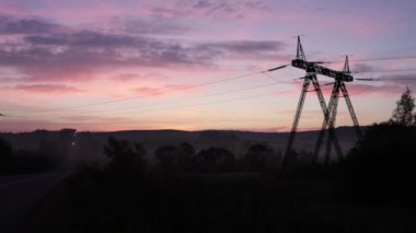 Gündoğumu silueti, elektrik şebekesi, elektrik kuleleri. Manzara, tarlalar arasında elektrik iletimi için gerekli kabloları taşıyan çelik kulelerle benekli..
