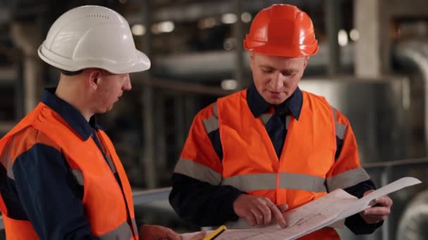 计划更新 工厂布局 设备蓝图 在生产设施内 工程师和工人共同评估施工蓝图 — 图库视频影像