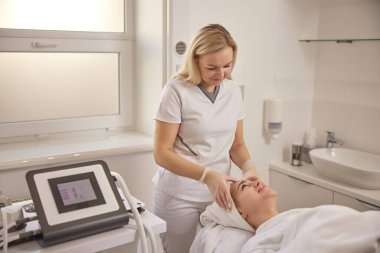 Eldiven, kozmetoloji kliniği, ince çizgiler. Güzellik kliniğindeki müşteri yetenekli kadın kozmetikçiden yüz masajı alıyor..
