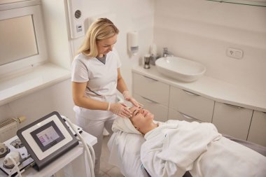 Kadın kozmetik uzmanı, spa masajı, akıl sağlığı uzmanı. Güzellik kliniğinin huzurlu ortamında kozmetolojide yetenekli bir kadın müşterilerine yüz masajı yapar..