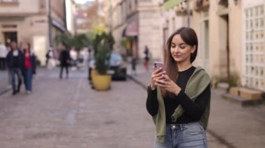 Akıllı telefon fotoğrafçılığı, kadın fotoğrafçılık, açık hava görüntüleri. Sokakta yürürken, güzel genç bir kadın cep telefonuyla fotoğraf çekiyor..