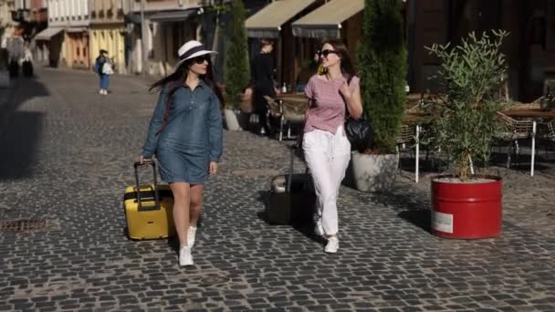 两个女人 旅行者散步 旅程快乐 两个可爱的女环球骑手在城市小道上漫步 身边拿着手提箱 享受着出国旅行的乐趣 — 图库视频影像