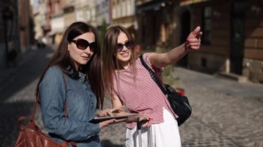 Gadget Seyahat, doğru yön, haritaya bakmak. Yönlendirme için tablet kullanan iki kadın turist senaryosu modern keşiflerin özünü ifade ediyor..