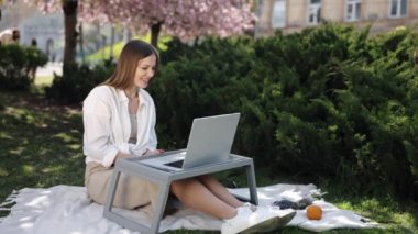 Laptop, açık hava çalışma alanı, uzaktan kumanda. Sakura ağacının altından, kadın dışarıda dizüstü bilgisayarıyla görüntülü sohbet yapıyor..