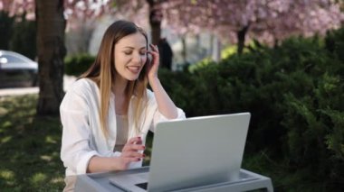 Sosyal uzaklık, Sakura parkı, video görüşmesi. Sakura ağacının altında, kadın dışarıda, bilgisayarından konuşurken görüntülendi..