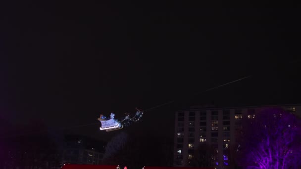 サンタクロース 眠りに乗る クリスマス シティスケープ サンタクロースは クリスマスシーズン中に妖精のクリスマスマーケットの上を飛ぶ彼らのトナカイに乗って ギフトボックスで彼らのスリーイに見られます — ストック動画