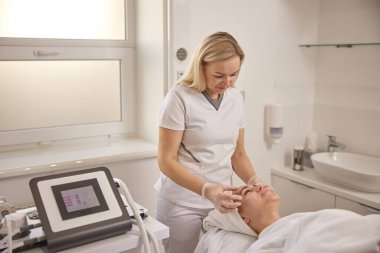 Güzellik merkezi, masaj tedavisi, spa merkezi. Güzellik kliniği, güzel bir kadın güzellik koltuğunda yüz masajı yaptırıyor sırt üstü uzanıyor, yüz masajı yaptırıyor, kafasında havlular, cilt bakımı ve kaplıca kavramlarıyla.