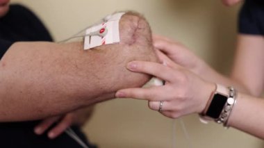 Rehabilitasyon araçları, iyileştirme teknolojisi, terapi aletleri. Profesyonel terapist, erkek hastaların kollarına elektroterapi uyguluyor, son model rehabilitasyon ekipmanlarını kullanıyor.