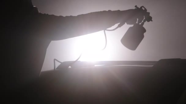 スプレーガン プロフェッショナルサービス ペイント耐久性 間違った雰囲気の中で バックライトは焦点のシルエットの人スプレーの絵画車に持って来ます — ストック動画