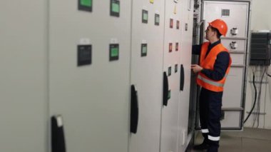 İşçi çalışıyor, kontrol paneli, panel teftişi. Fabrikada, elektrikçi çoklu metrenin yardımıyla kontrol panelindeki elektrik akımını analiz ediyor..