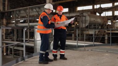 Taslak tartışması, yapısal çalışma, fabrika çizimi. Fabrikanın derinliklerinde, teknik taslak hem mühendis hem de inşaatçının dikkatini çekiyor..