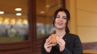 Açık hava yemeği, Burger zamanı, koyu saçlı tüketici. Esmer saçlı genç bir kadın lokantanın hemen dışında hamburgerle yemek yiyor..