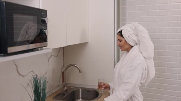 洗完澡 健康小口 健康厨房 穿着浴衣的妇女在厨房里喝着洁净的水 体现了精神健康的营养 — 图库视频影像