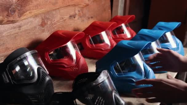 保护面具 彩弹战斗 游戏用具 将红蓝相间的彩色球面具排在木制架子上 在开始游戏前 玩家会从架子上取下面具 — 图库视频影像