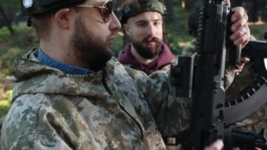 Lasertag arenası, oyun brifingi, stratejik toplantı. Laser Tag yarışmacılarını topluyor, kamuflaj kıyafetleri giyiyor ve her biri sürükleyici işaretler taşıyor, aktif olarak orman manzarasında yer alıyor.