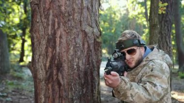 Askeri hassasiyet, etiket nişancısı, doğal ortam. Orman düzeninde, kamuflajlı bir adam kafasında işaretle ağaca yaslanır, lazer tabancasını hedef alır ve düşmana ateş eder..