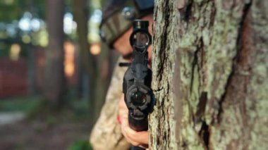 Kamuflaj tüfeği, orman çatışması, nişan alma. Orman ortamında, kafasında işaretle kamuflaj kıyafeti giymiş bir adam ağaca karşı ustalıkla lazer tabancasını hedefliyor.