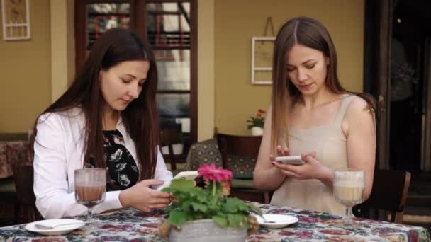 ストリートカフェ 座っている女性 ソーシャルネットワーク カフェに座っている2人の女性が 個々の電話会話に集まって — ストック動画