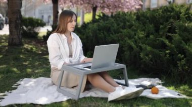 Çevrimiçi sohbet, Sakura manzarası, dijital göçebe. Çiçekli sakura ağacının arkasında, kadın açık havada dizüstü bilgisayarıyla video tartışmasına giriyor..