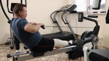 Protez ekipman, uzuv eğitimi, spor salonu egzersizi. Yapay bacaklı bir adam spor salonunda kürek çekiyor..