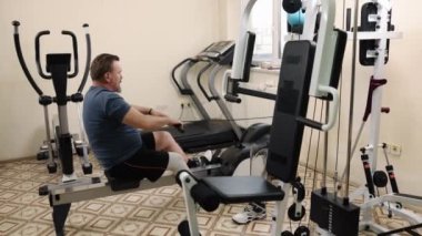 Spor salonu, fitness merkezi, uyarlanabilir fitness. Antrenman tesisinde protez bacaklı bir adam kürek çekerken görülüyor..