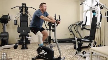 Beden eğitimi, spor aletleri, eğitim adaptasyonu. Yapay bacaklı adam spor salonunda bacak pres makinesinde çalışıyor. Etrafı çeşitli ekipmanlarla çevrili..