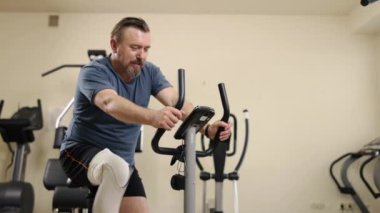 Uyum sağlama, ekipman kullanımı, protez eğitimi. Protez bacaklı adam fitness merkezinde bacak pres makinesi kullanıyor, diğer egzersiz ekipmanlarıyla çevrili..