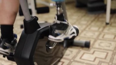 Dayanıklılık eğitimi, protez rutini, egzersiz adaptasyonu. Protez bacaklı bir adam spor salonunda bacak egzersizi yapar. Etrafı sayısız fitness makinesiyle çevrilidir..