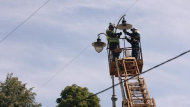 İşçi onarımı, montaj sırasında, metal direk. Sokak lambası tamiri, tepedeki sokak lambasını tamir eden işçiler, yeni lamba montajı, elektrik direği tamir eden işçiler.
