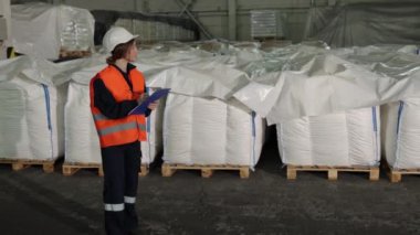 Fabrika teftişi, çanta sayma, mal teftişi. Fabrika kadın müfettişi ürünleri inceler, beyaz çuvalları sayar ve gözlemlerini kaydeder..