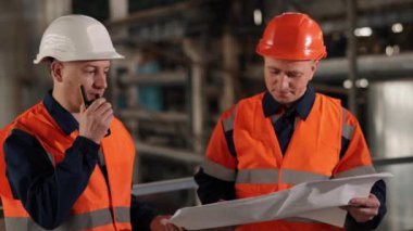 Konsültasyon çizmek, şemaları incelemek, çizelgeleri okumak. Tartışmanın derinliklerinde, mühendis ve inşaat uzmanı fabrika içindeki tasarımları analiz ediyor.
