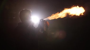 Alev yaratıcılığı, ateş sanatları, yangın önlemleri. Sisli ortamda gölgeli bir figür, korunmak için gaz maskesi takarak ateş püskürten sprey kullanıyor..