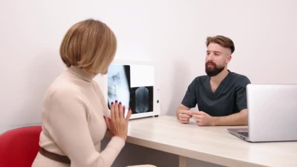 X線ディスカッション イメージング分析 放射線分析 男性の医師は 診療現場で女性患者とX線の結果を議論し ラップトップとライトボックスが見える — ストック動画