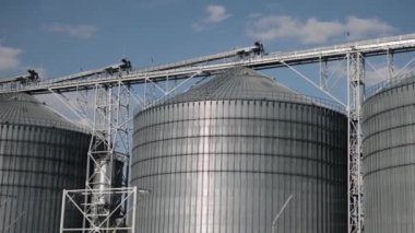 Endüstriyel bağlantı, Silo tesisi, metal endüstrisi. Canlı mavi gökyüzünün altında, metalik tahıl ambarları daha büyük bir endüstriyel tesise sabitlenmiştir..
