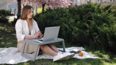 Zaman geçirmek, park konferansı, serbest meslek hayatı. Dışarda oturmuş, Sakura ağacını çerçeveliyor, kadın bilgisayarındaki video çağrısına dalmış durumda..