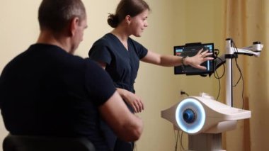 Uyum sorunu, robot yardımcıları, tıbbi robotlar. Erkek hasta, terapi seansı sırasında yüksek teknolojili robotik ekipman kullanan konsantre fizyoterapistten kol egzersizi yardımı alıyor..