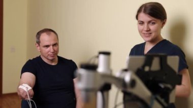Engelli insanlar, terapi teknolojisi, rehabilitasyon teknolojisi. Klinik seansta fizyoterapist, kolu için robotik destekli egzersizleri olan bir adama özenle yardım ediyor..