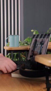 Laptop, yeşil çizgiler, tahta arka plan. Erkek eller dizüstü bilgisayarı alırken yakın çekimdir, ahşap masa üzerinde mavi kupa ve dikey arka plan çizgili duvar ve yeşil santral, dikey video.