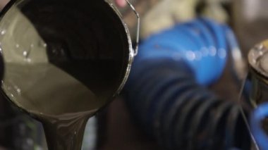 Erkek ressam, boya sıvısı, boya aletleri. Erkek sanatçı boyayı metal bir kutudan diğerine yerleştiriyor..