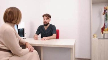 Manuel terapi, klinik toplantı, anatomi modelleri. Erkek fizyoterapist klinikteki hastaya danışmanlık yapıyor. Arkalarında da anatomik model bulunuyor..