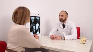Klinik Tartışması, Radyoloji İncelemesi, Tıbbi Muayene. Beyaz önlüklü erkek doktor, klinikteki kadın hastayla omurilik röntgeni görüntülerini gözden geçiriyor..