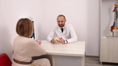 Hasta değerlendirmesi, tıbbi raf, tedavi planı. Hasta durumunu tartışan fizyoterapist, ayrıntıları daha açık bir şekilde açıklamak için raftaki anatomik modeli işaret ediyor..