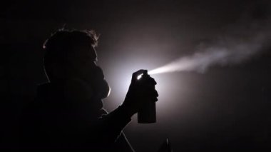 Sanatsal yangın, güvenlik protokolleri, yangın gösterisi. Kasvetli, sisli uzay sisli silueti koruma amaçlı gaz maskesi takan sprey kutusuyla ustaca ateş püskürtüyor..