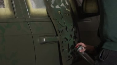 Gaz maskesi, araç tamiri, restorasyon işçiliği. Özenli bir şekilde, gaz maskeli şahıs otomobil yüzeyine boya uyguluyor ve otomotiv yenilemesindeki ustalığını gösteriyor..