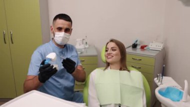 Diş kalıbı, diş anksiyetesi, diş tavsiyeleri. Yüz maskesi takan diş hekimi, dişçi koltuğunda oturan kadına tedavi planını anlatırken model ve aletler gösteriyor.