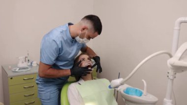 Oral muayene, diş bakımı, diş muayenesi. Diş sandalyesinde oturan kadın diş hekimi ağız retraktörünü, mavi önlüklü dişçiyi diş muayenesi yaparken tespit eder..