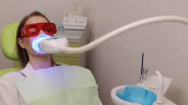 Mavi ışık, dişçi ekipmanları, diş muayenesi. Diş kliniğinde, hasta mavi ışık cihazıyla diş beyazlatma işlemi sırasında koruyucu gözlük takıyor..