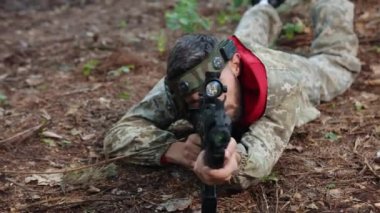 Kamuflaj teçhizatı, taktik eğitimi, nişancı eğitimi. Orman eğitim ortamında, lazer nişancı kamuflaj teçhizatıyla dümdüz uzanır, hassas görüşe sahip paintball silahıyla dikkatlice nişan alır..